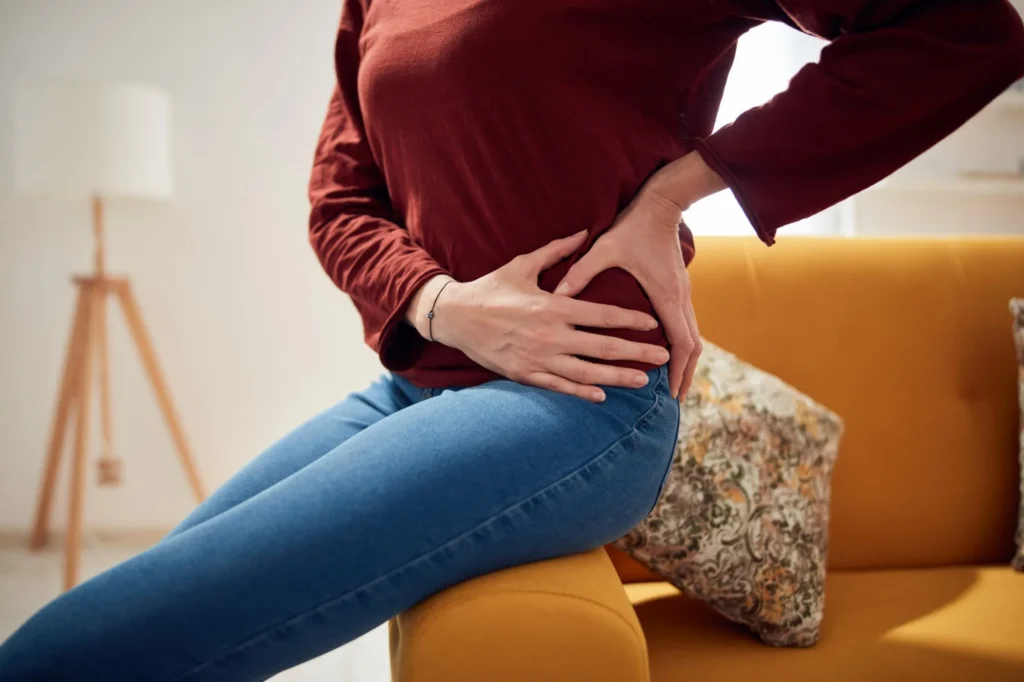 Woman holding her hip in pain while seated on a sofa